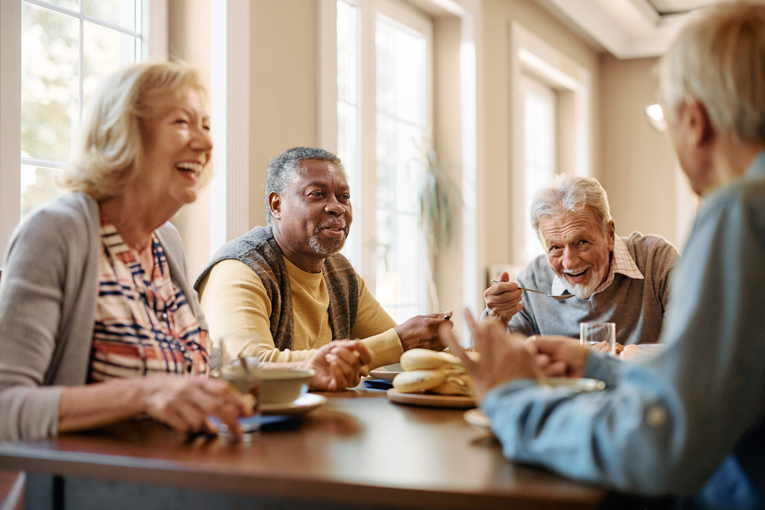 Happy African American senior man talking to his friends while eating at dining table at nursing home.